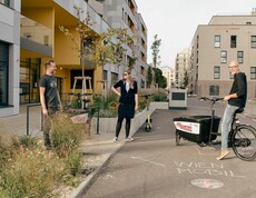Zwei Personen stehen nebeneinander, ein Mann steht neben ihnen mit einem Lastenfahrrad