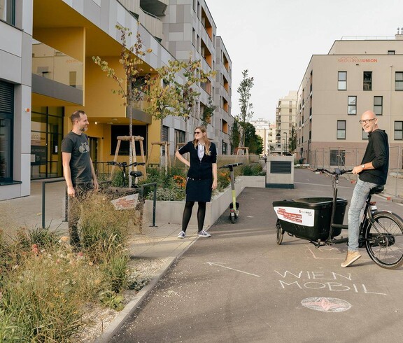 Zwei Personen stehen nebeneinander, ein Mann steht neben ihnen mit einem Lastenfahrrad