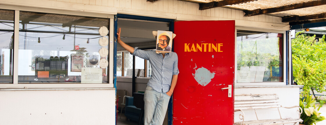 Mann mit einem Gesichtsfoto vor seinem Gesicht steht an der Tür einer Kantine