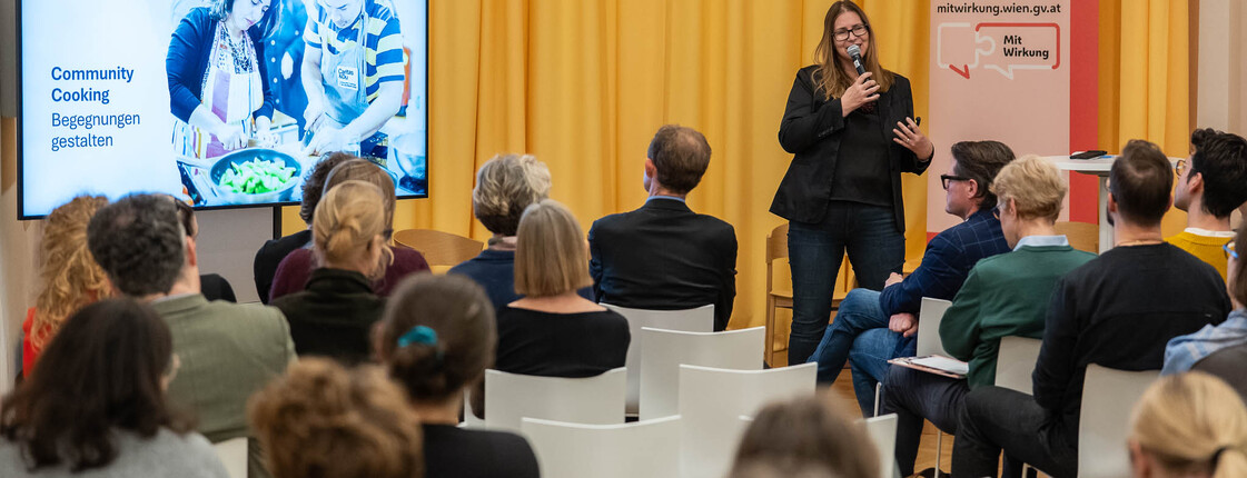 eine Frau steht vor Menschen die auf Sessel sitzen