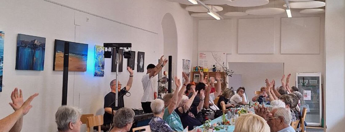 Senior:innen an einem Tisch setzen und singen zusammen